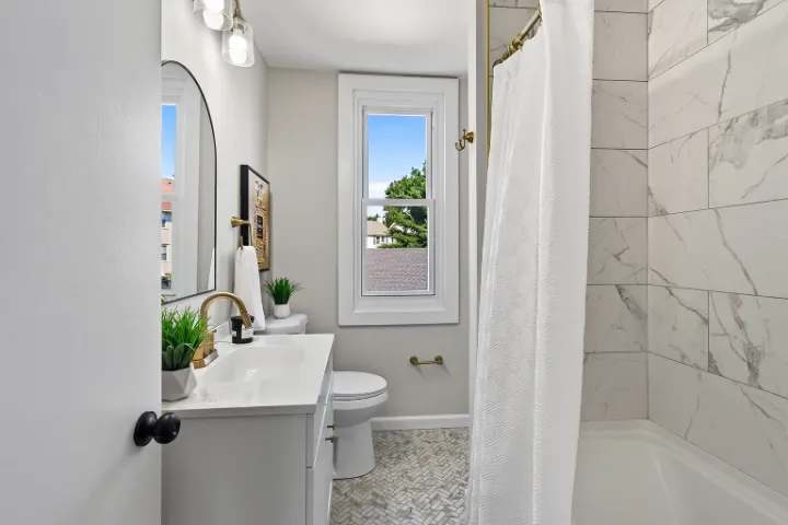 Renovated bathroom with marble-look tile, herringbone floor, and brass fixtures
