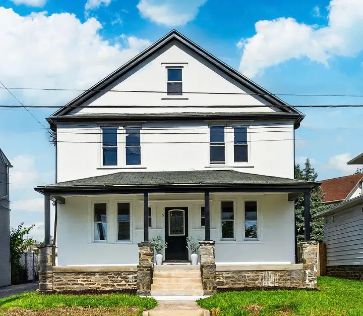 Front of the house after renovation: white stucco, black porch columns and front door